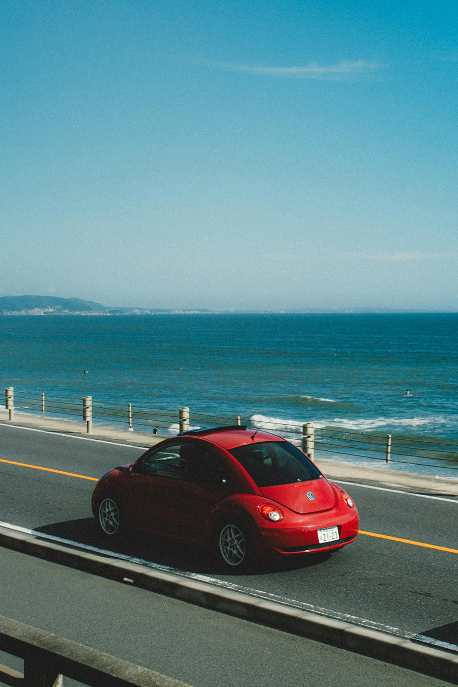 red car driving along beach road